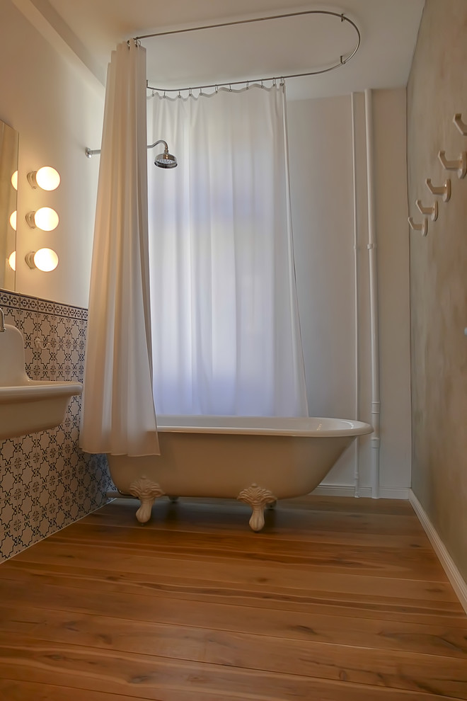 Foto på ett mellanstort vintage en-suite badrum, med ett badkar med tassar, en dusch/badkar-kombination, en vägghängd toalettstol, grå väggar, målat trägolv, brunt golv, dusch med duschdraperi, vit kakel, keramikplattor och ett väggmonterat handfat