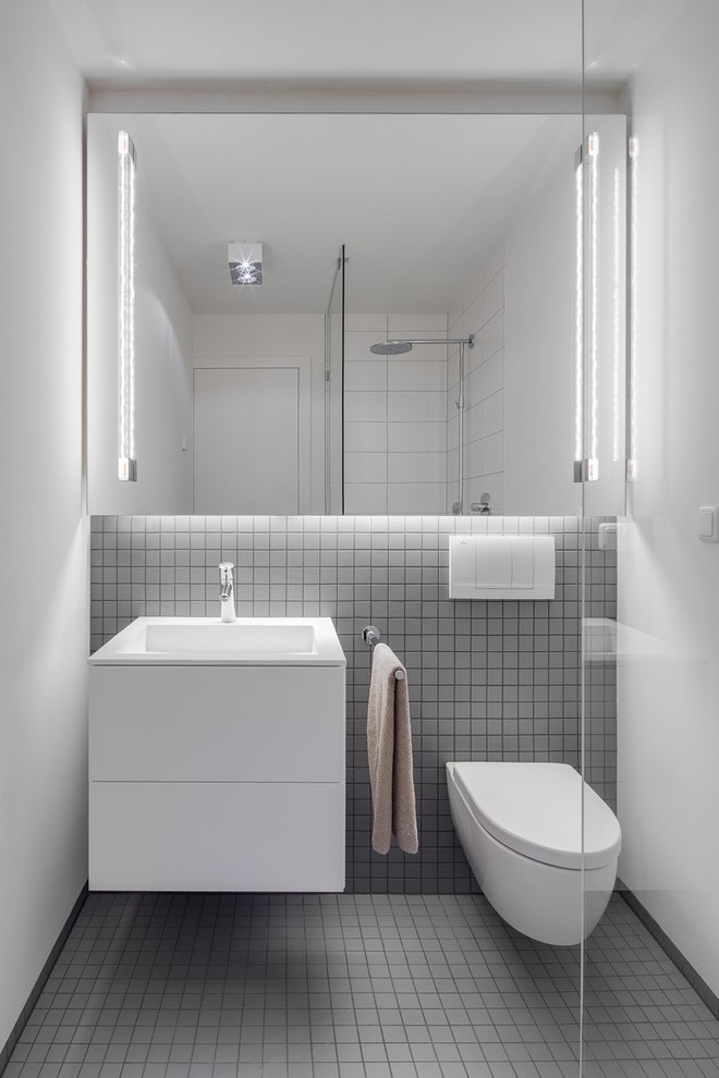 Diseño de cuarto de baño contemporáneo pequeño con armarios con paneles lisos, puertas de armario blancas, ducha esquinera, sanitario de pared, baldosas y/o azulejos grises, baldosas y/o azulejos de cerámica, paredes blancas y lavabo integrado