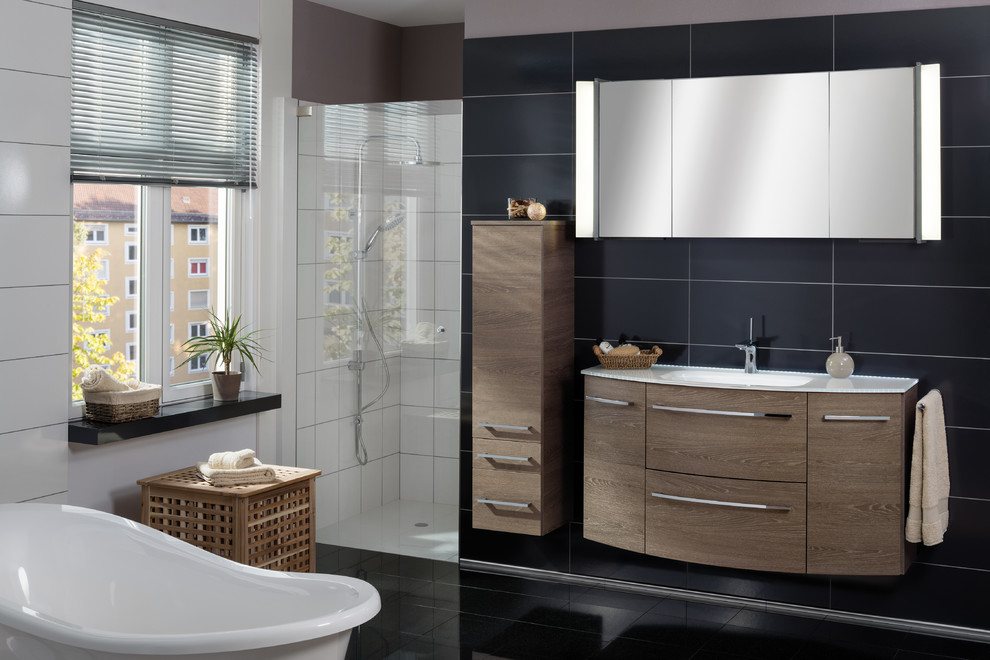 Inspiration for a large contemporary bathroom in Nuremberg with dark wood cabinets, a trough sink, glass worktops, flat-panel cabinets, a freestanding bath, an alcove shower, black tiles, ceramic tiles, white walls, ceramic flooring, black floors and a hinged door.
