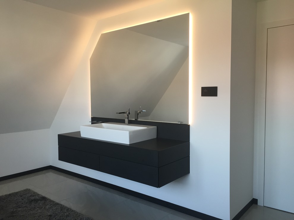 Свежая идея для дизайна: ванная комната в современном стиле с плоскими фасадами, черными фасадами, белыми стенами, настольной раковиной и зеркалом с подсветкой - отличное фото интерьера
