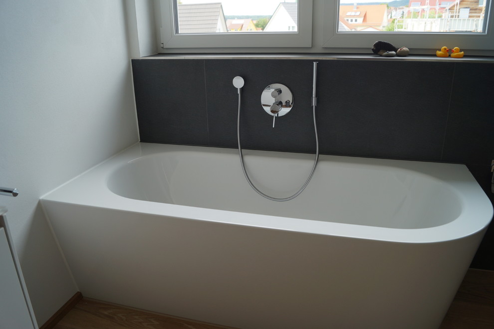 Photo of a large contemporary ensuite bathroom in Stuttgart with flat-panel cabinets, white cabinets, a built-in bath, a built-in shower, a wall mounted toilet, grey tiles, stone tiles, grey walls, medium hardwood flooring, a trough sink and glass worktops.