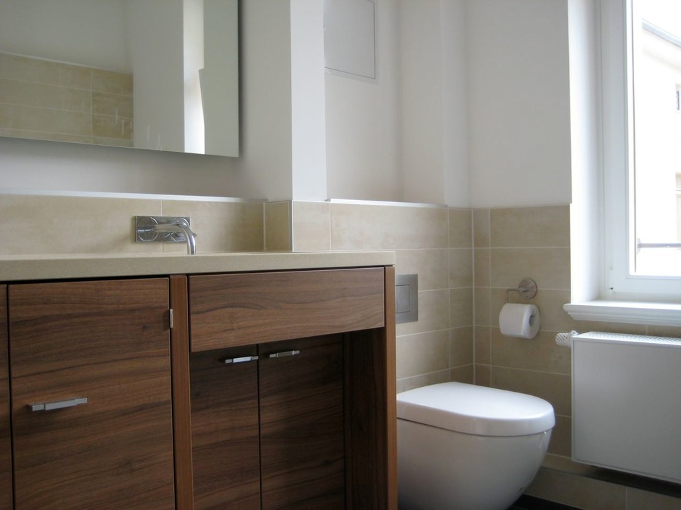Diseño de cuarto de baño principal clásico renovado pequeño con armarios con paneles lisos, puertas de armario de madera en tonos medios, bañera encastrada, ducha a ras de suelo, sanitario de pared, baldosas y/o azulejos beige, paredes blancas, lavabo integrado y encimera de acrílico