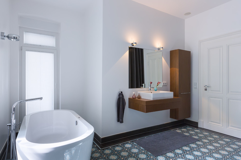 This is an example of a large contemporary ensuite bathroom in Cologne with a vessel sink, flat-panel cabinets, a freestanding bath, white walls, dark wood cabinets, a built-in shower, a wall mounted toilet, cement flooring, wooden worktops, turquoise floors and an open shower.