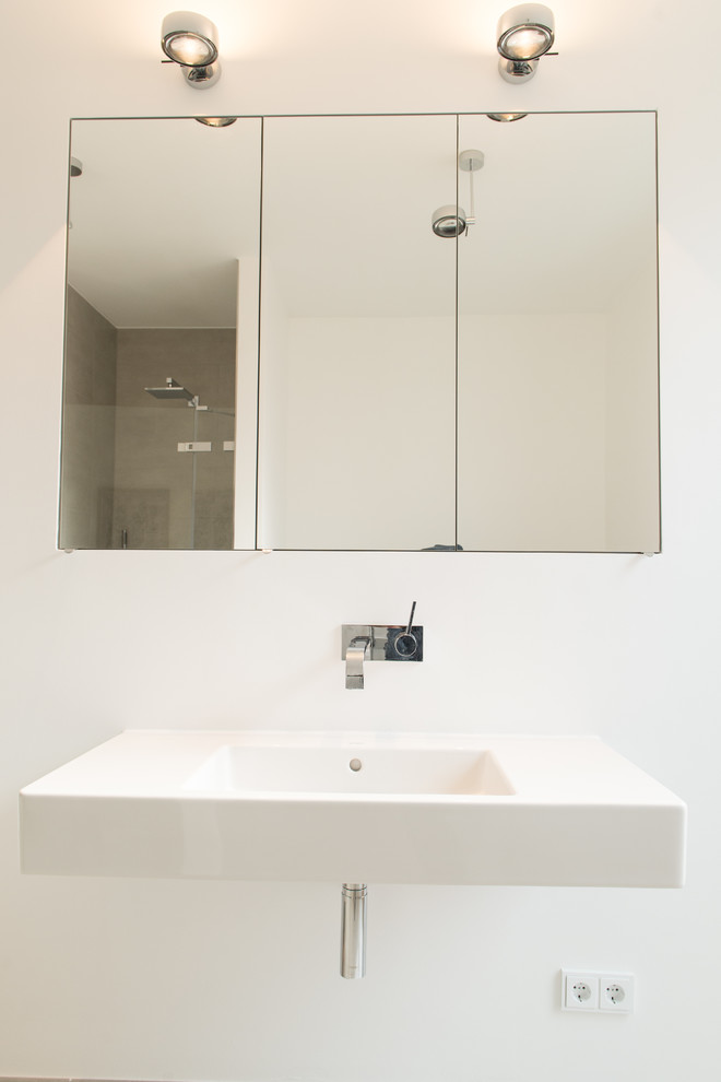 Inredning av ett modernt mellanstort en-suite badrum, med vit kakel, ett fristående badkar, en kantlös dusch, en vägghängd toalettstol, vita väggar, öppna hyllor, glaskakel, mörkt trägolv, ett väggmonterat handfat, bänkskiva i akrylsten, brunt golv och dusch med skjutdörr