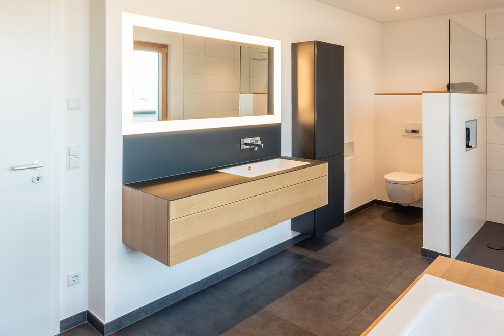 Exemple d'une salle de bain moderne de taille moyenne avec un placard à porte plane, des portes de placard marrons, WC suspendus, un mur blanc, un lavabo posé, un plan de toilette en bois, un sol gris et aucune cabine.