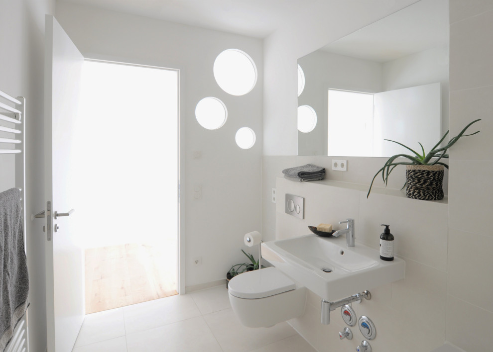 Cette image montre une petite salle d'eau design avec une baignoire posée, un combiné douche/baignoire, WC suspendus, un carrelage beige, des carreaux de porcelaine, un mur blanc, un sol en carrelage de porcelaine, un lavabo suspendu, un sol beige et une cabine de douche avec un rideau.