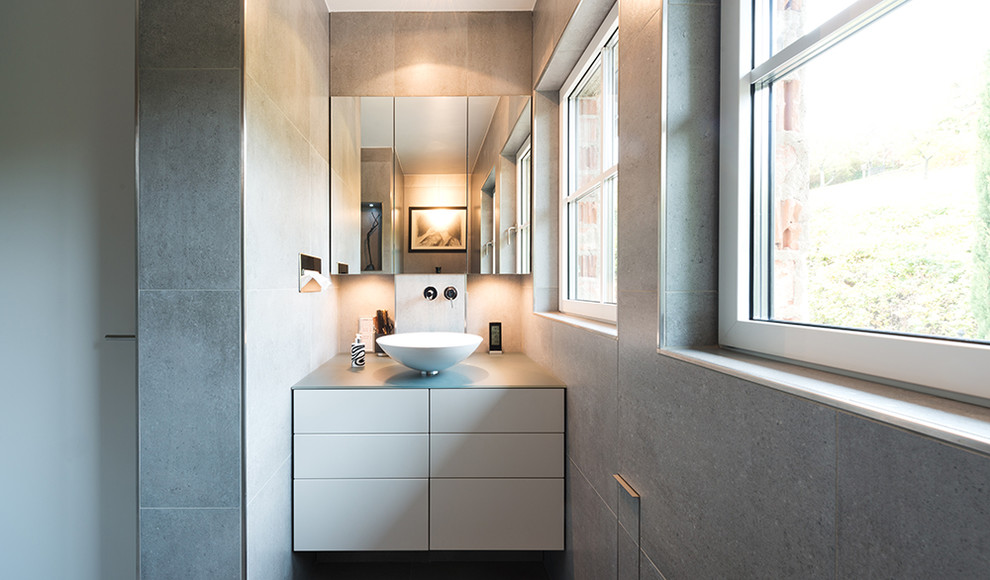 Modernes Badezimmer mit flächenbündigen Schrankfronten, weißen Schränken, grauen Fliesen, Aufsatzwaschbecken und Steinfliesen in Berlin