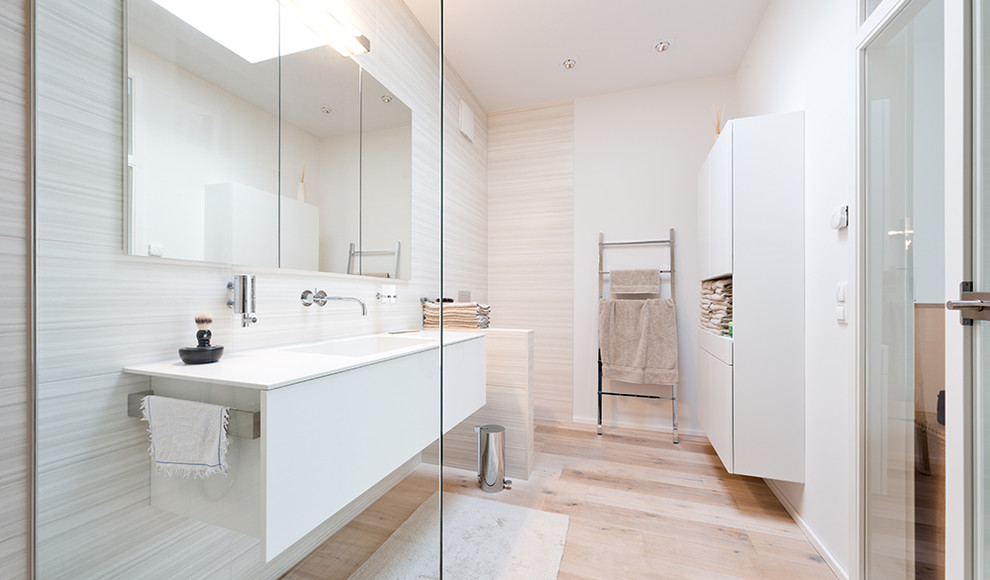 Foto de cuarto de baño actual con armarios con paneles lisos, puertas de armario blancas, paredes blancas, suelo de madera clara y lavabo integrado