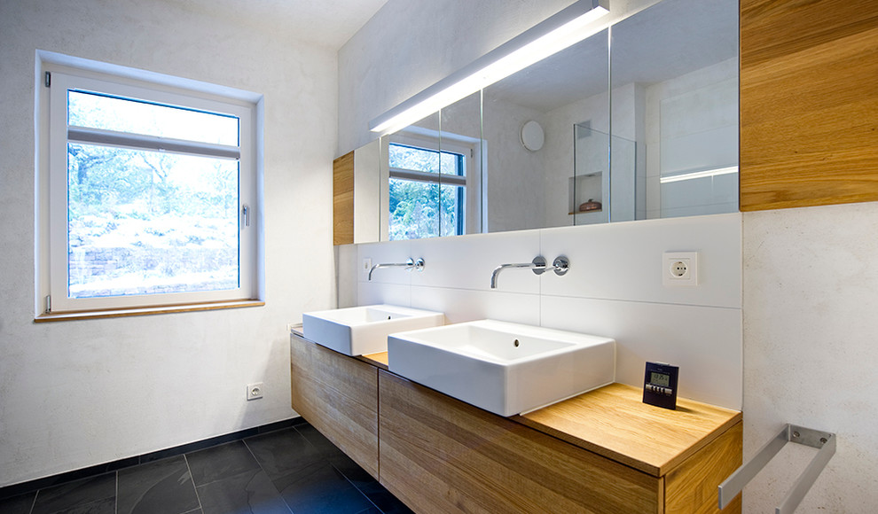 Modernes Badezimmer mit flächenbündigen Schrankfronten, hellbraunen Holzschränken, weißer Wandfarbe, Aufsatzwaschbecken und weißen Fliesen in Berlin