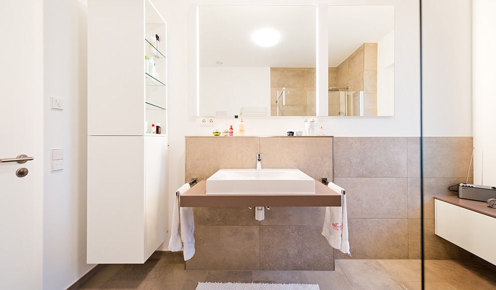 Aménagement d'une salle de bain contemporaine avec un placard à porte plane, des portes de placard blanches, un carrelage beige, un mur blanc, une vasque, une douche d'angle et des dalles de pierre.