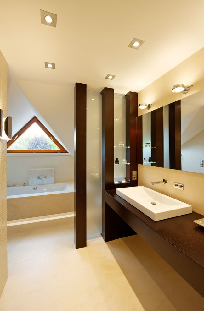 Réalisation d'une grande salle de bain design en bois foncé avec une vasque, un placard à porte plane, un plan de toilette en bois, une baignoire posée et un mur beige.