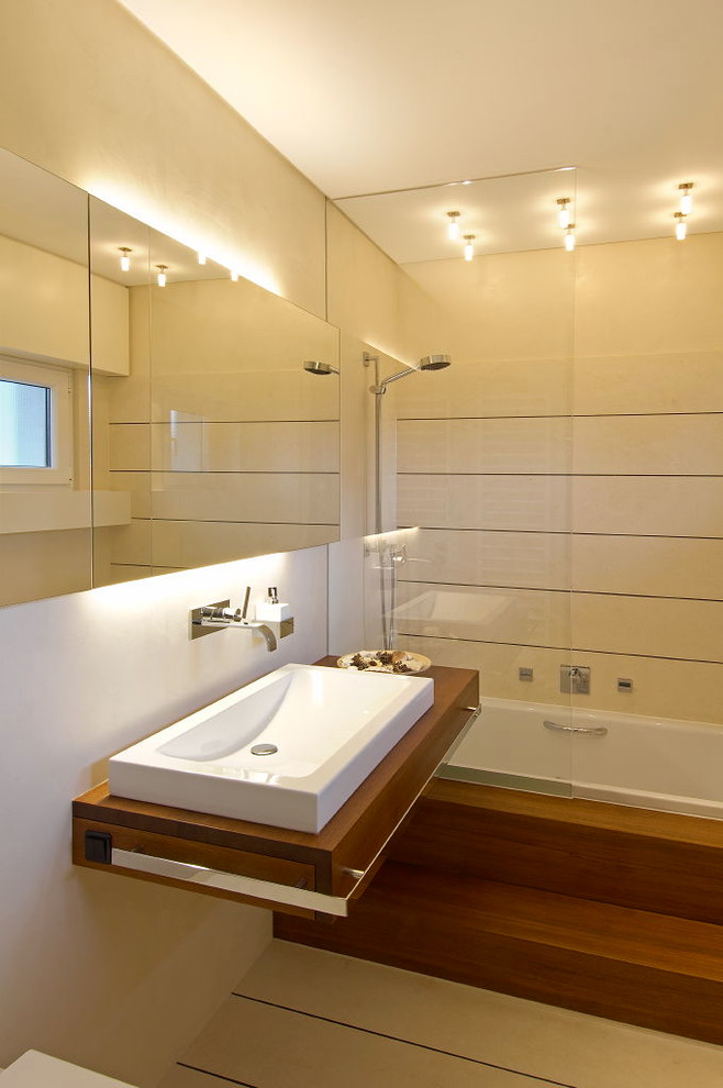 Immagine di una stanza da bagno contemporanea di medie dimensioni con lavabo a bacinella, top in legno, vasca da incasso, piastrelle beige, pareti beige e vasca/doccia