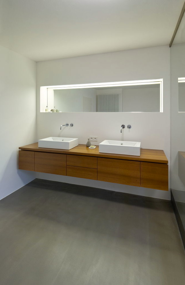 Großes Modernes Badezimmer mit Aufsatzwaschbecken, flächenbündigen Schrankfronten, hellbraunen Holzschränken, Waschtisch aus Holz, weißer Wandfarbe und Betonboden in Köln