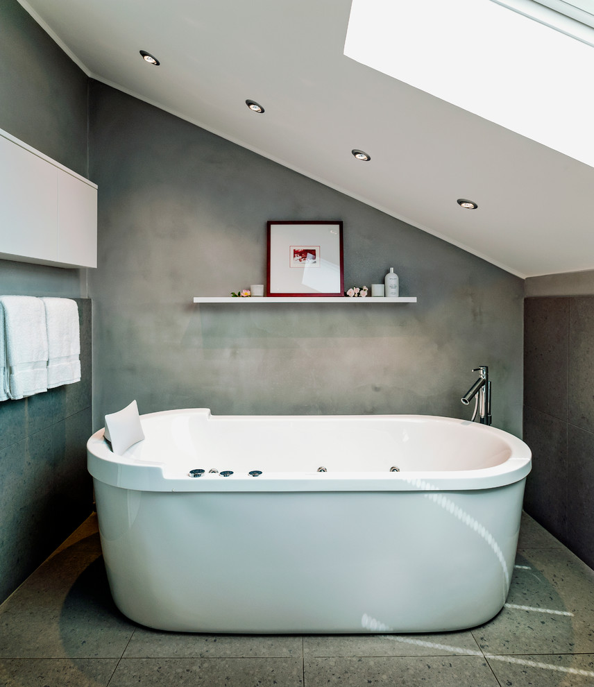 Imagen de cuarto de baño contemporáneo de tamaño medio con armarios con paneles lisos, puertas de armario blancas, bañera exenta, baldosas y/o azulejos grises, losas de piedra y paredes grises