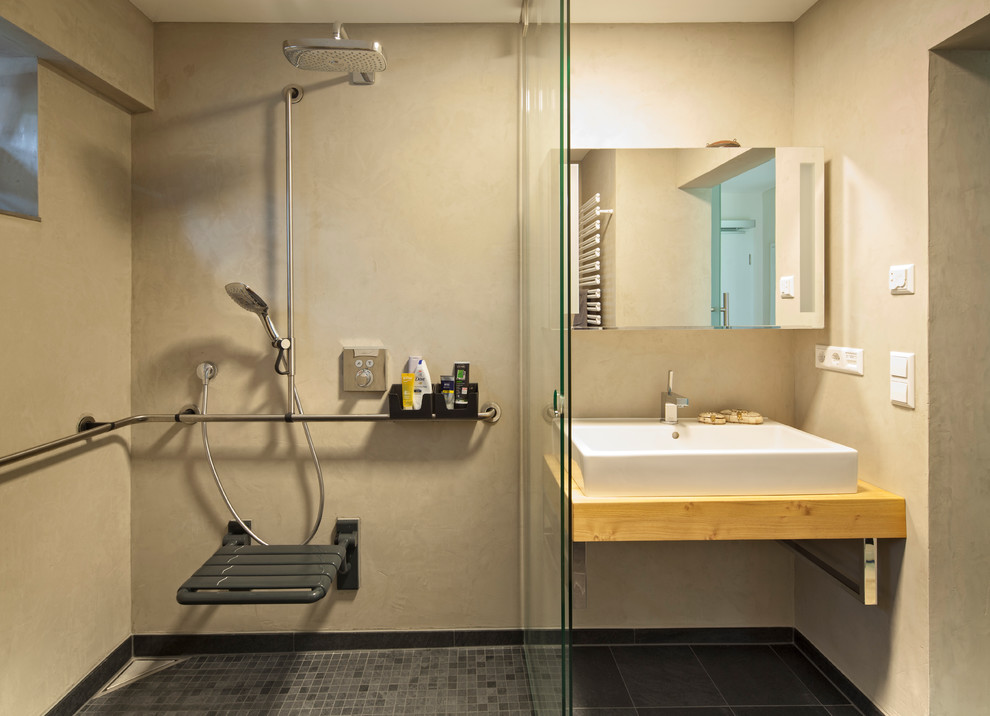 Imagen de cuarto de baño contemporáneo de tamaño medio con ducha a ras de suelo, sanitario de pared, baldosas y/o azulejos grises, paredes grises, aseo y ducha, lavabo sobreencimera y encimera de madera