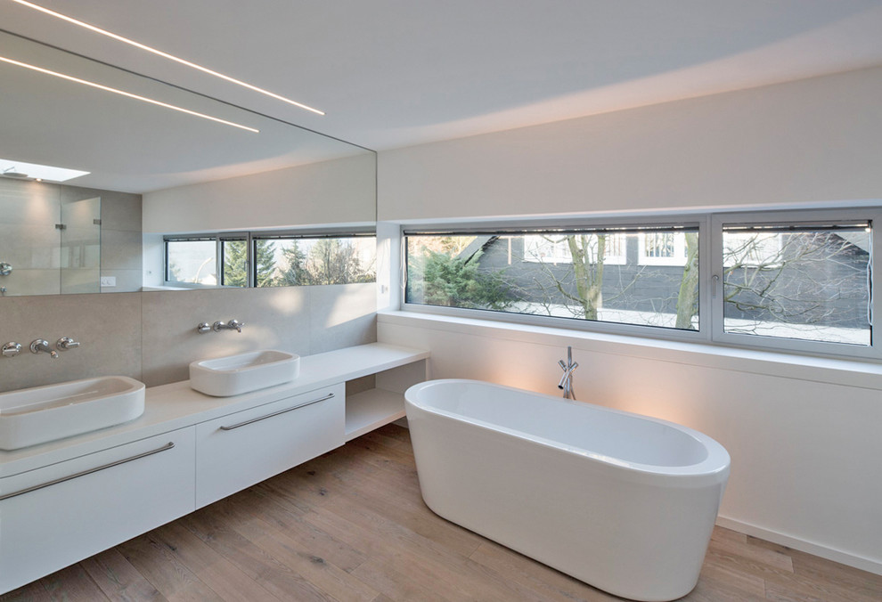 デュッセルドルフにある高級な広いコンテンポラリースタイルのおしゃれなマスターバスルーム (ベッセル式洗面器、フラットパネル扉のキャビネット、白いキャビネット、置き型浴槽、白い壁、無垢フローリング) の写真