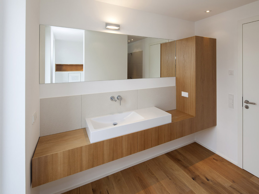 Cette photo montre une salle de bain moderne en bois brun de taille moyenne avec une vasque, un placard à porte plane, un carrelage gris, un mur blanc, un sol en bois brun et un plan de toilette en bois.
