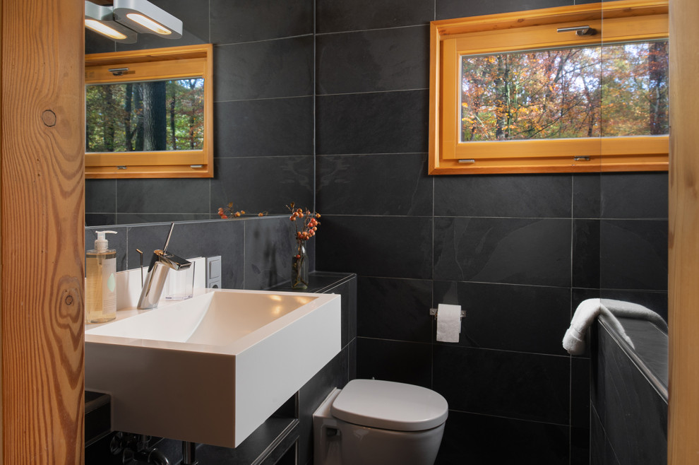Diseño de cuarto de baño único rústico de tamaño medio con sanitario de pared, baldosas y/o azulejos negros, baldosas y/o azulejos de porcelana, aseo y ducha y lavabo suspendido