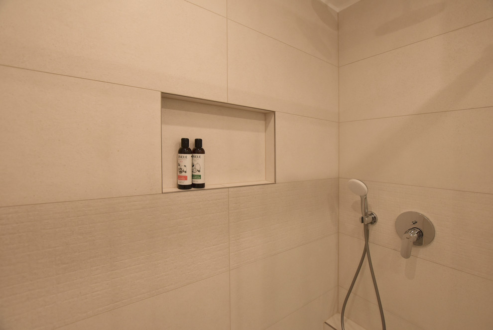 Modern inredning av ett litet badrum med dusch, med en dusch i en alkov, en vägghängd toalettstol, beige kakel, keramikplattor, beige väggar, klinkergolv i porslin, ett väggmonterat handfat, brunt golv och dusch med skjutdörr
