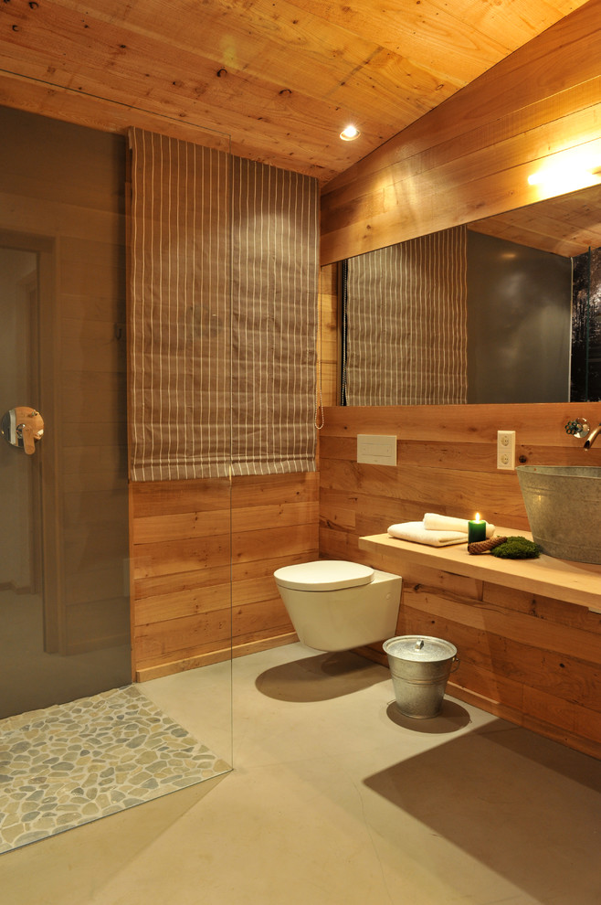 Idee per una stanza da bagno con doccia rustica di medie dimensioni con doccia ad angolo, piastrelle di ciottoli, lavabo a bacinella, WC sospeso, top in legno, pareti marroni, doccia aperta e top marrone