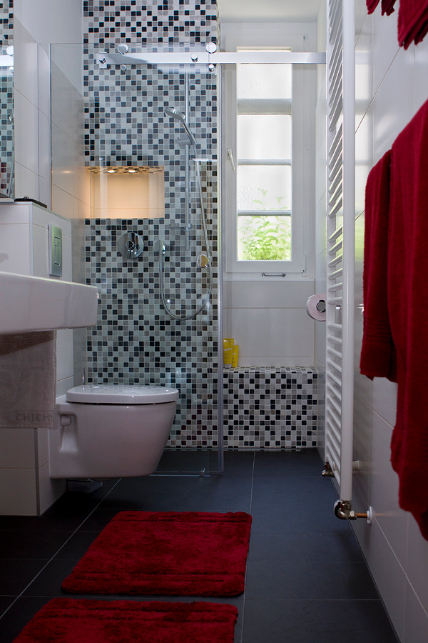 Idéer för ett modernt badrum, med släta luckor, skåp i mörkt trä, en dusch i en alkov, en vägghängd toalettstol, svart och vit kakel, mosaik, vita väggar, klinkergolv i keramik, ett väggmonterat handfat, svart golv och dusch med skjutdörr