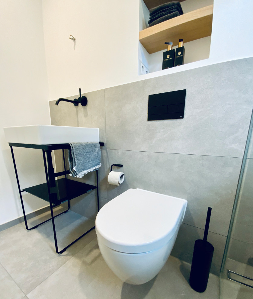 Kleines Modernes Duschbad mit Wandtoilette, grauen Fliesen, weißer Wandfarbe, Wandwaschbecken, schwarzer Waschtischplatte, Wandnische, Einzelwaschbecken und freistehendem Waschtisch in Sonstige