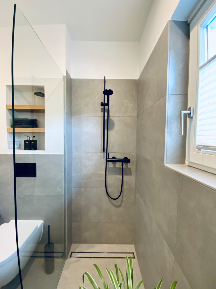 Ejemplo de cuarto de baño único y de pie actual pequeño con sanitario de pared, baldosas y/o azulejos grises, paredes blancas, aseo y ducha, lavabo suspendido, encimeras negras y hornacina