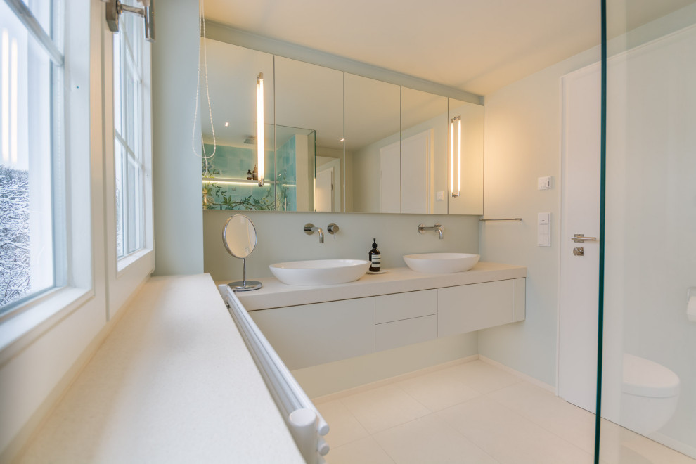 Modern inredning av ett mellanstort vit vitt badrum med dusch, med blå kakel, keramikplattor, beige väggar, klinkergolv i keramik, ett väggmonterat handfat, beiget golv, släta luckor och vita skåp