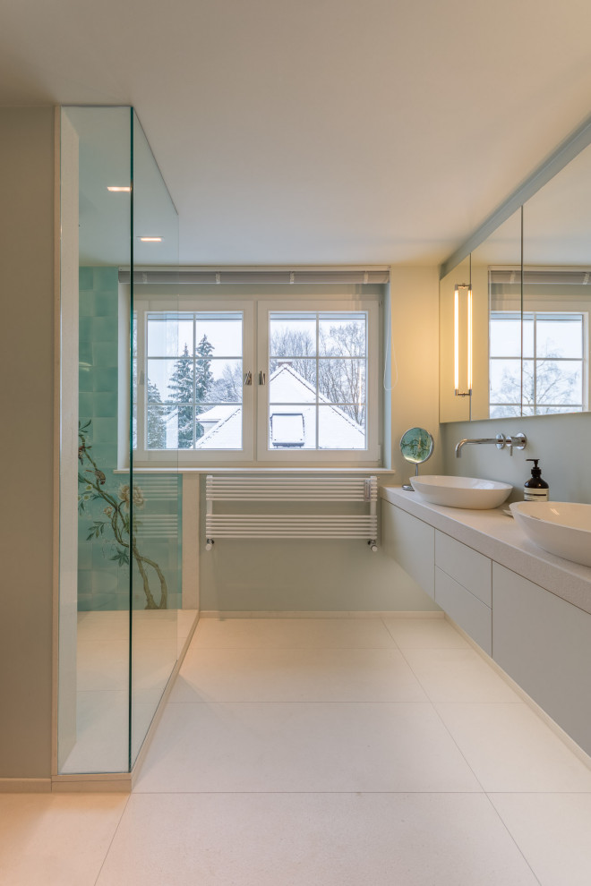 На фото: ванная комната среднего размера в современном стиле с душем над ванной, синей плиткой, керамической плиткой, бежевыми стенами, полом из керамической плитки, душевой кабиной, подвесной раковиной, бежевым полом и белой столешницей