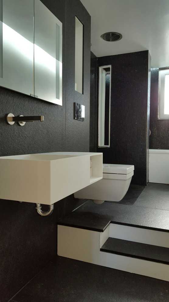 Idée de décoration pour une salle de bain minimaliste de taille moyenne avec une baignoire en alcôve, une douche à l'italienne, WC suspendus, un carrelage noir, un carrelage de pierre, un mur noir, un lavabo suspendu, un plan de toilette en surface solide, un sol noir et une cabine de douche à porte battante.