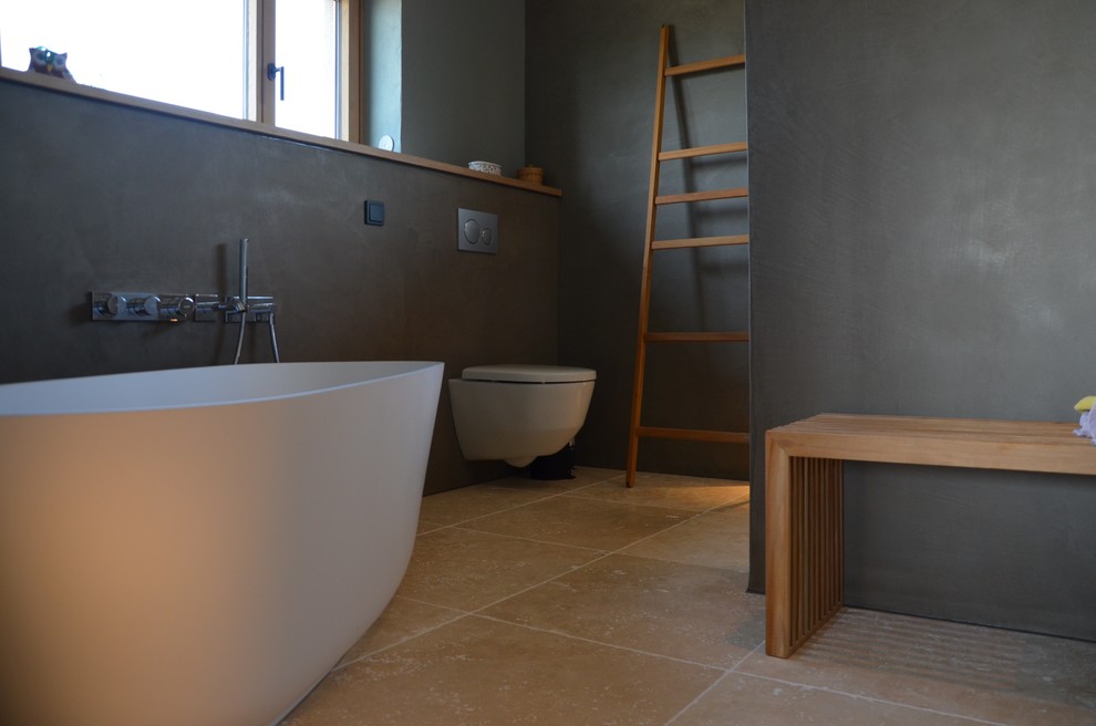 Idée de décoration pour une grande salle de bain principale design avec une baignoire indépendante, une douche à l'italienne, un mur gris, un sol en travertin, aucune cabine et WC suspendus.