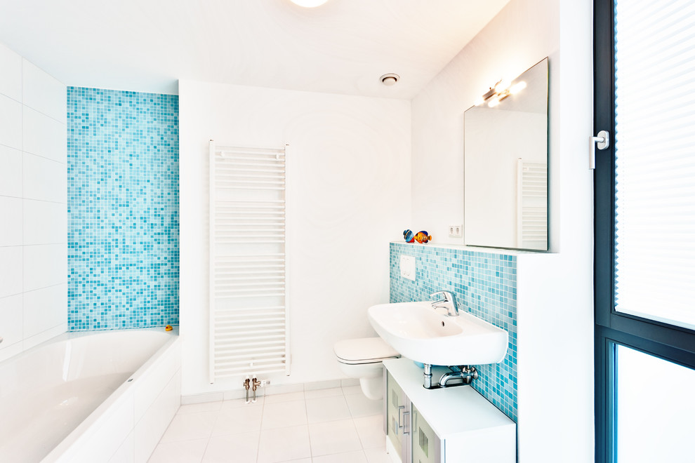 Inspiration för små moderna badrum, med vita skåp, ett platsbyggt badkar, blå kakel, vita väggar, klinkergolv i porslin, en vägghängd toalettstol, mosaik, ett väggmonterat handfat och släta luckor
