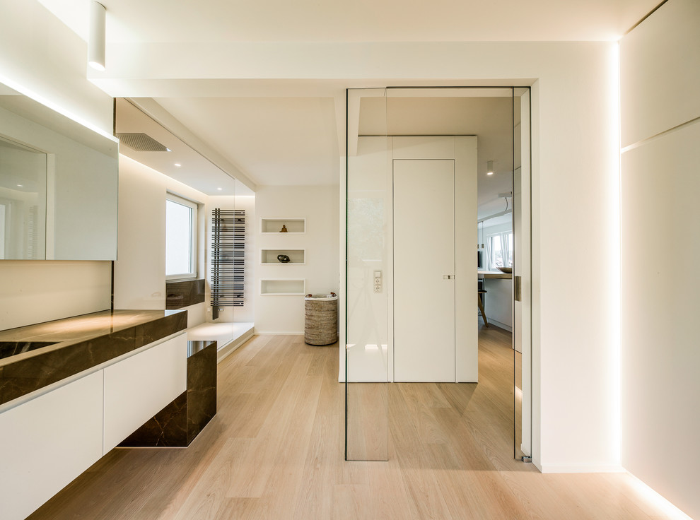 Diseño de cuarto de baño actual grande con armarios con paneles lisos, puertas de armario blancas, ducha abierta, paredes blancas, suelo de madera clara, lavabo integrado y ducha abierta