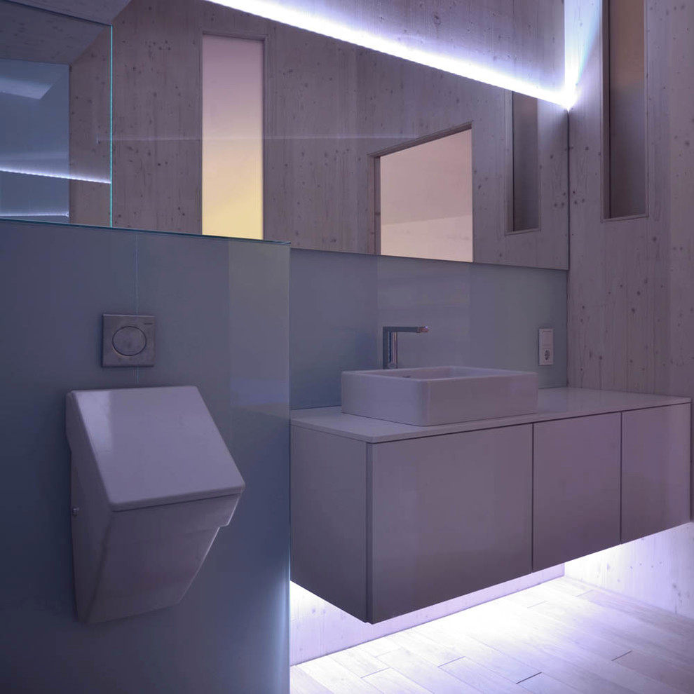 Bild på ett mellanstort funkis badrum med dusch, med släta luckor, vita skåp, en kantlös dusch, ett urinoar, vit kakel, glasskiva, beige väggar, ett fristående handfat och laminatbänkskiva