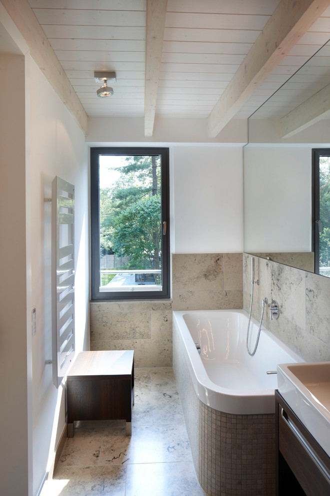 Modern inredning av ett badrum, med skåp i mörkt trä, ett hörnbadkar, stenkakel, vita väggar, ett fristående handfat, träbänkskiva och marmorgolv