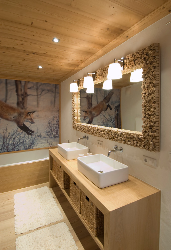 Foto på ett mellanstort rustikt badrum, med ett fristående handfat, ett badkar i en alkov, vita väggar, ljust trägolv och träbänkskiva