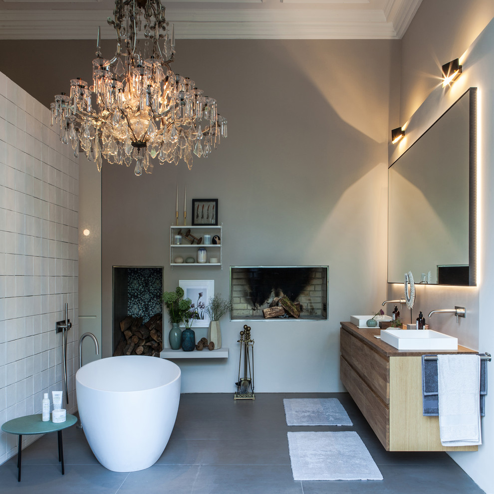 Photo of a large contemporary ensuite bathroom in Hamburg with flat-panel cabinets, light wood cabinets, a freestanding bath, a built-in shower, a wall mounted toilet, white tiles, limestone tiles, beige walls, ceramic flooring, a built-in sink, solid surface worktops, grey floors, an open shower and brown worktops.
