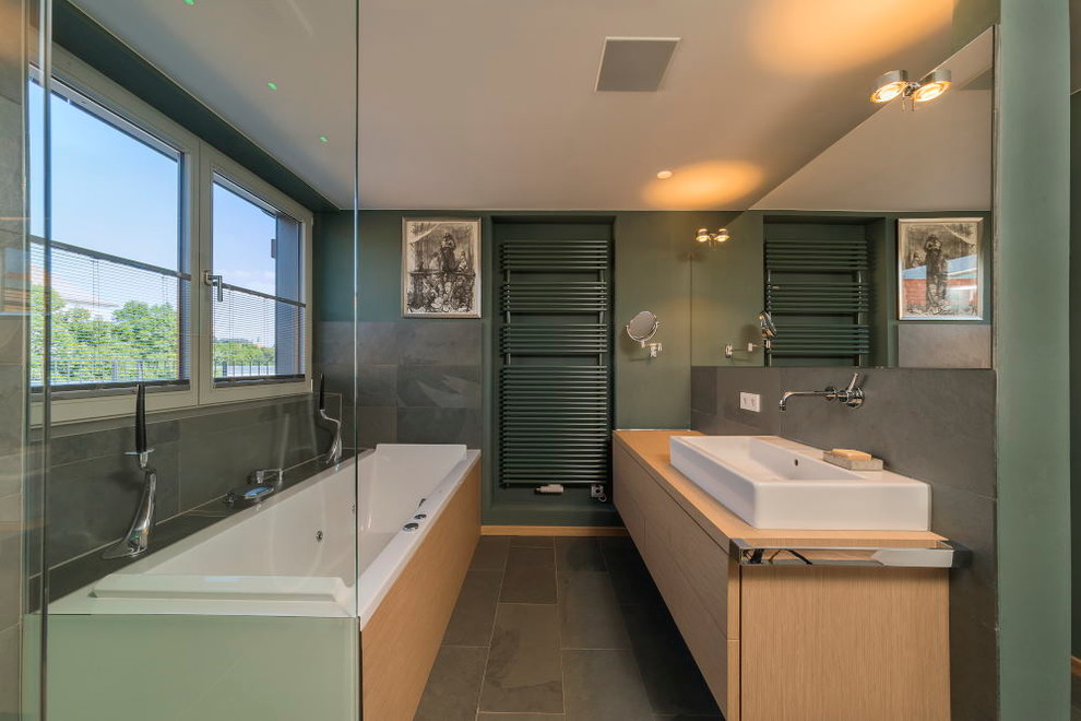 This is an example of a medium sized contemporary bathroom in Dresden with flat-panel cabinets, medium wood cabinets, a built-in bath, grey tiles, stone slabs, green walls, slate flooring, a vessel sink and wooden worktops.