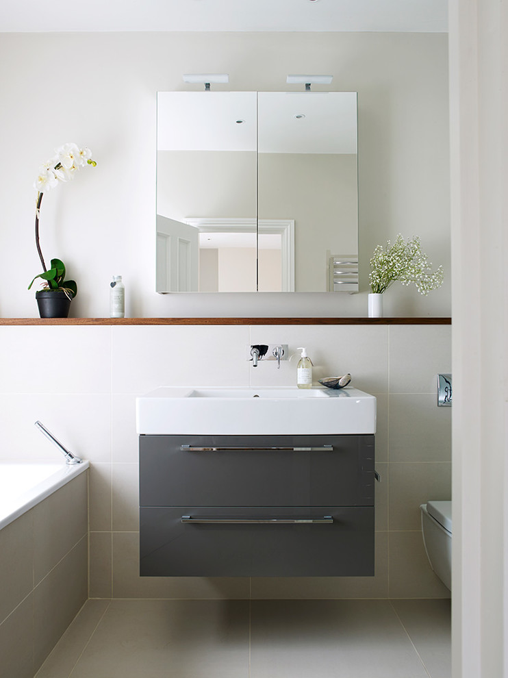Modernes Badezimmer mit flächenbündigen Schrankfronten, grauen Schränken, Badewanne in Nische, grauen Fliesen, grauer Wandfarbe, Waschtischkonsole und Wandtoilette in Sonstige