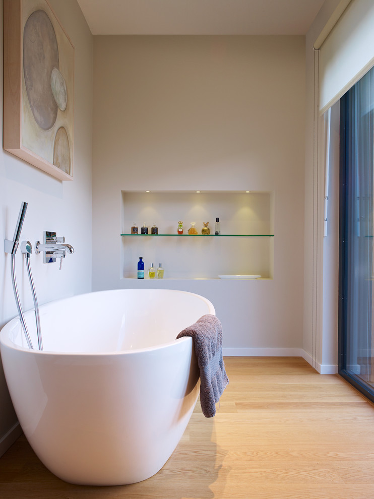 Modern inredning av ett mellanstort badrum, med ett fristående badkar, vita väggar och mellanmörkt trägolv