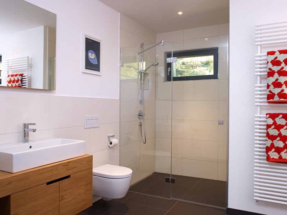 Exempel på ett litet modernt badrum, med släta luckor, skåp i mellenmörkt trä, en dusch i en alkov, en vägghängd toalettstol, beige kakel, keramikplattor, vita väggar, ett fristående handfat och träbänkskiva