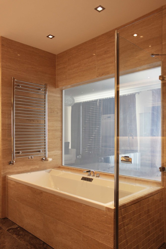Immagine di una stanza da bagno contemporanea con vasca da incasso, piastrelle beige e piastrelle in pietra