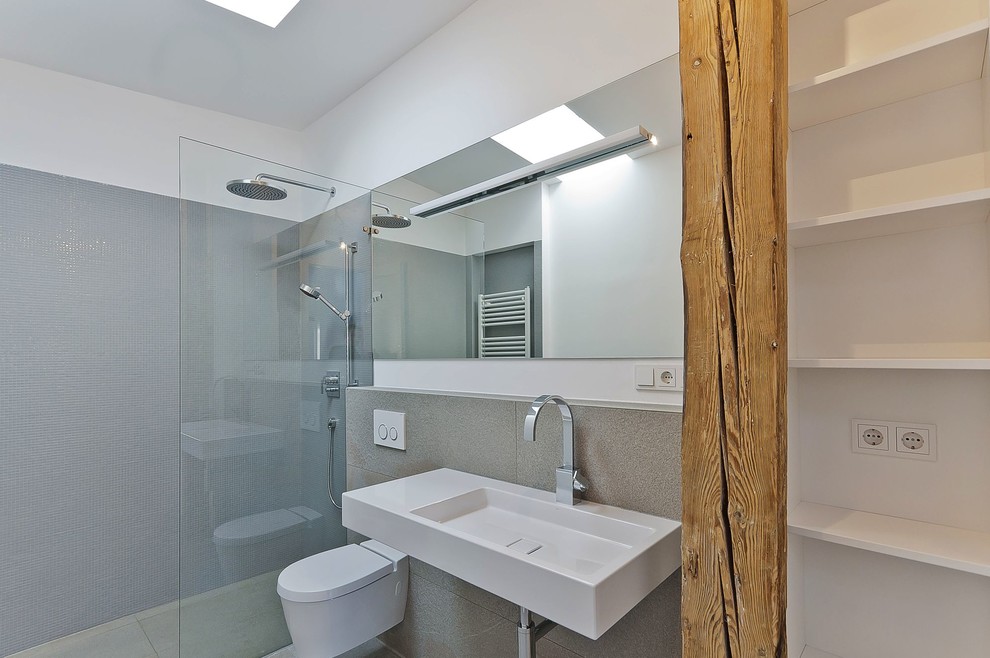 Kleines Modernes Duschbad mit offenen Schränken, bodengleicher Dusche, Wandtoilette, grauen Fliesen, weißer Wandfarbe und Wandwaschbecken in München