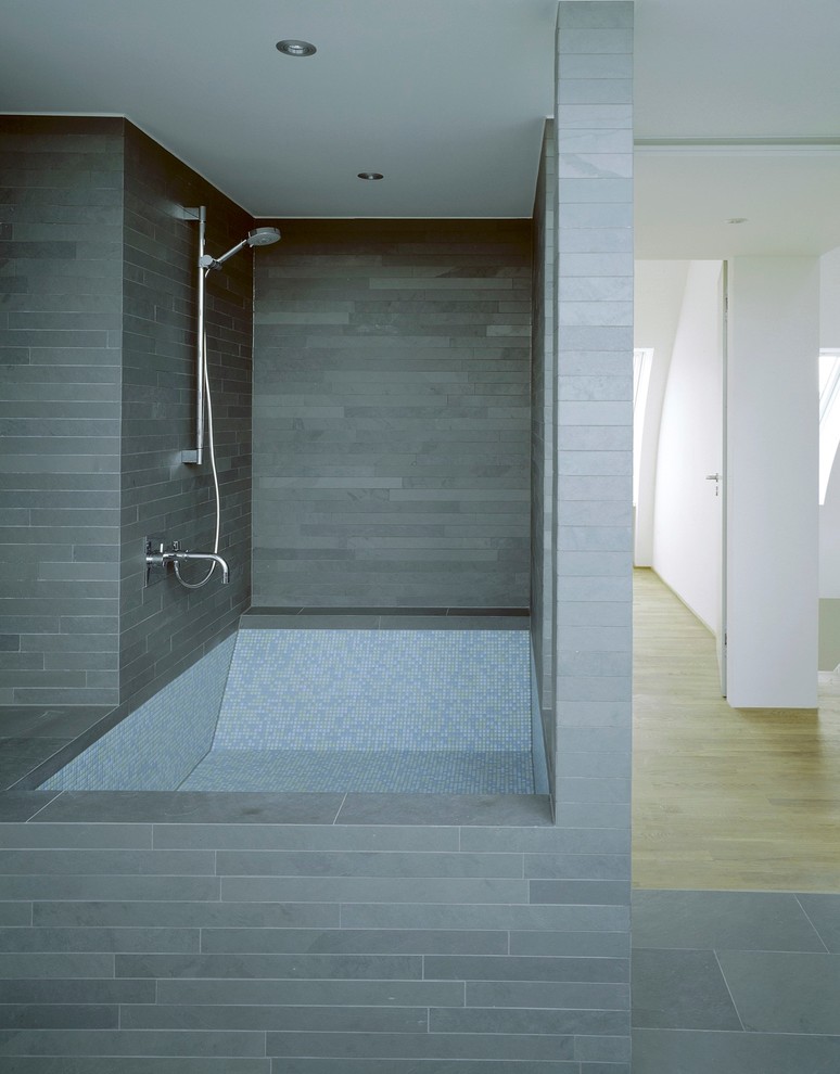 Foto di una stanza da bagno design con piastrelle grigie, vasca da incasso, vasca/doccia, piastrelle in pietra, pareti grigie e pavimento in ardesia