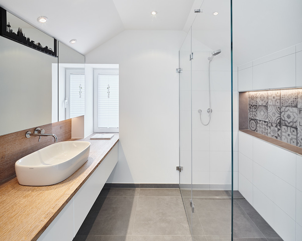 Пример оригинального дизайна: ванная комната в современном стиле с белыми фасадами, столешницей из дерева, душем без бортиков, серой плиткой, белой плиткой, настольной раковиной, белыми стенами, керамической плиткой и коричневой столешницей