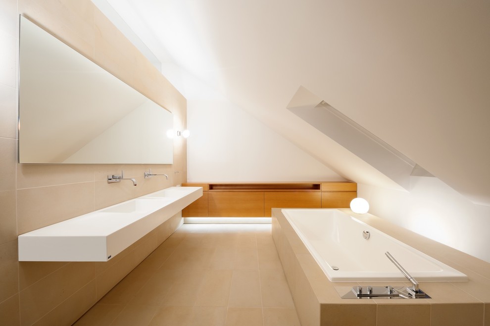 Ispirazione per una stanza da bagno moderna di medie dimensioni con lavabo integrato, ante lisce, ante in legno scuro, vasca da incasso, piastrelle beige, pareti bianche e piastrelle in pietra