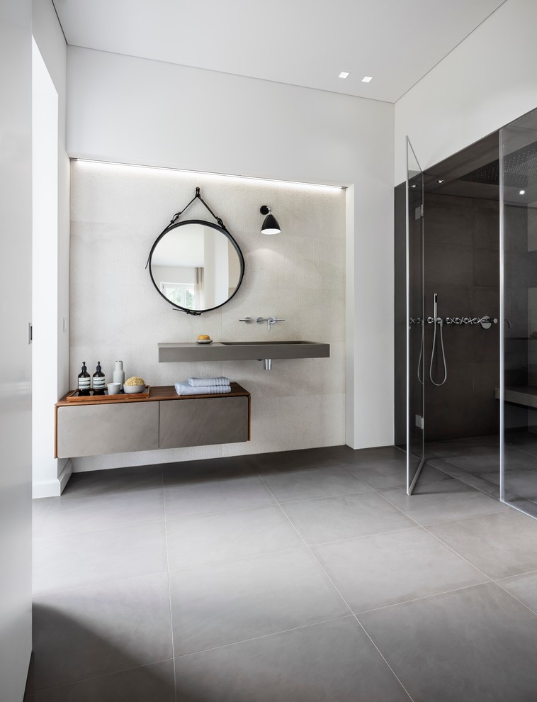Стильный дизайн: большая главная ванная комната в стиле модернизм с плоскими фасадами, серыми фасадами, душем без бортиков, раздельным унитазом, бежевой плиткой, плиткой из известняка, белыми стенами, полом из известняка, монолитной раковиной, столешницей из известняка, серым полом и серой столешницей - последний тренд