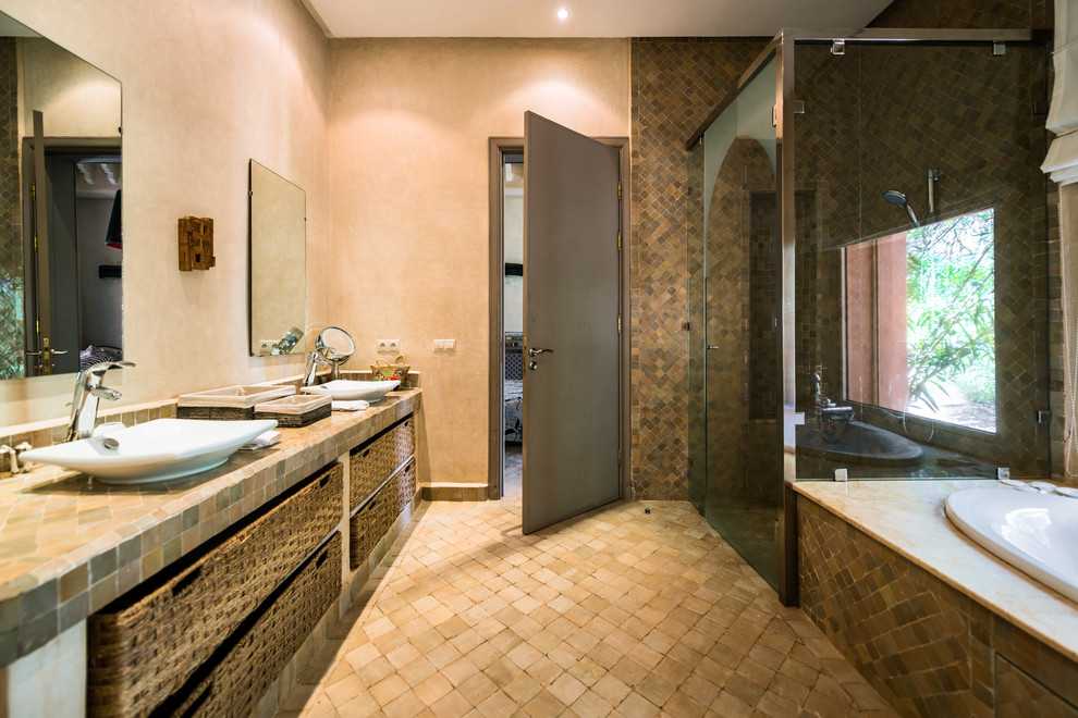 Пример оригинального дизайна: большая ванная комната в средиземноморском стиле с коричневыми фасадами, накладной ванной, душевой комнатой, коричневой плиткой, каменной плиткой, бежевыми стенами, полом из терракотовой плитки, душевой кабиной, настольной раковиной, коричневым полом и душем с распашными дверями