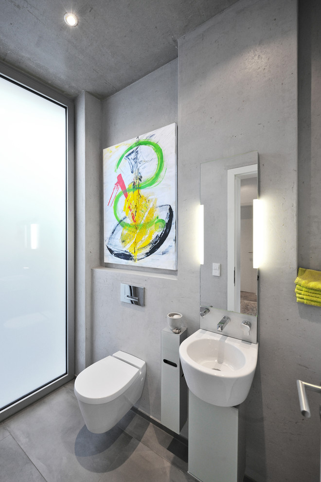 Modern inredning av ett litet vit vitt badrum, med en vägghängd toalettstol, grå väggar, betonggolv, släta luckor, ett fristående badkar, en kantlös dusch, grå kakel, cementkakel, ett konsol handfat, bänkskiva i akrylsten, grått golv och med dusch som är öppen