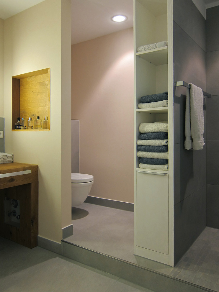 Diseño de cuarto de baño contemporáneo con lavabo sobreencimera, encimera de madera, bañera encastrada, ducha a ras de suelo, sanitario de pared, baldosas y/o azulejos grises, baldosas y/o azulejos de cerámica y suelo de baldosas de cerámica